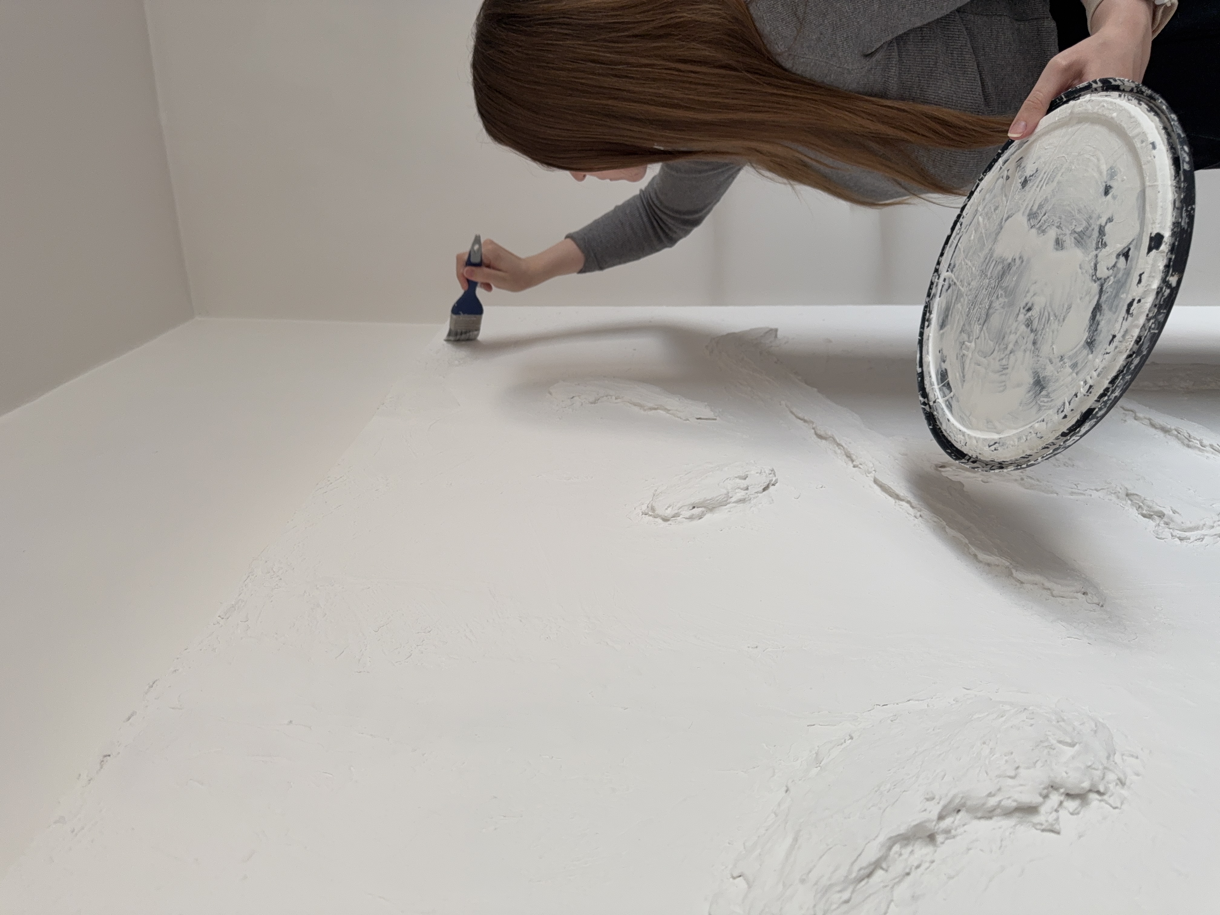 Behind the scenes photo of artist Jenny Halseid applying drywall mud to sculpt the Dao character.