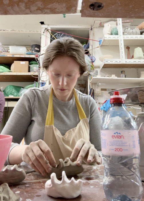 Hand-building a Knyttneve sculpture in the ceramics studio, shaping the clenched-fist form in stoneware clay before it's fired and glazed.